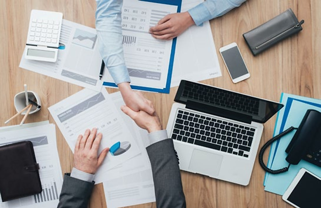 Two people shaking hands across a desk of business documents
